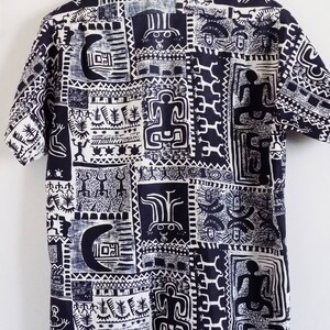 Pu&ograve; includere: Una camicia a maniche corte bianca e nera con un motivo geometrico. Il motivo presenta figure e simboli stilizzati.