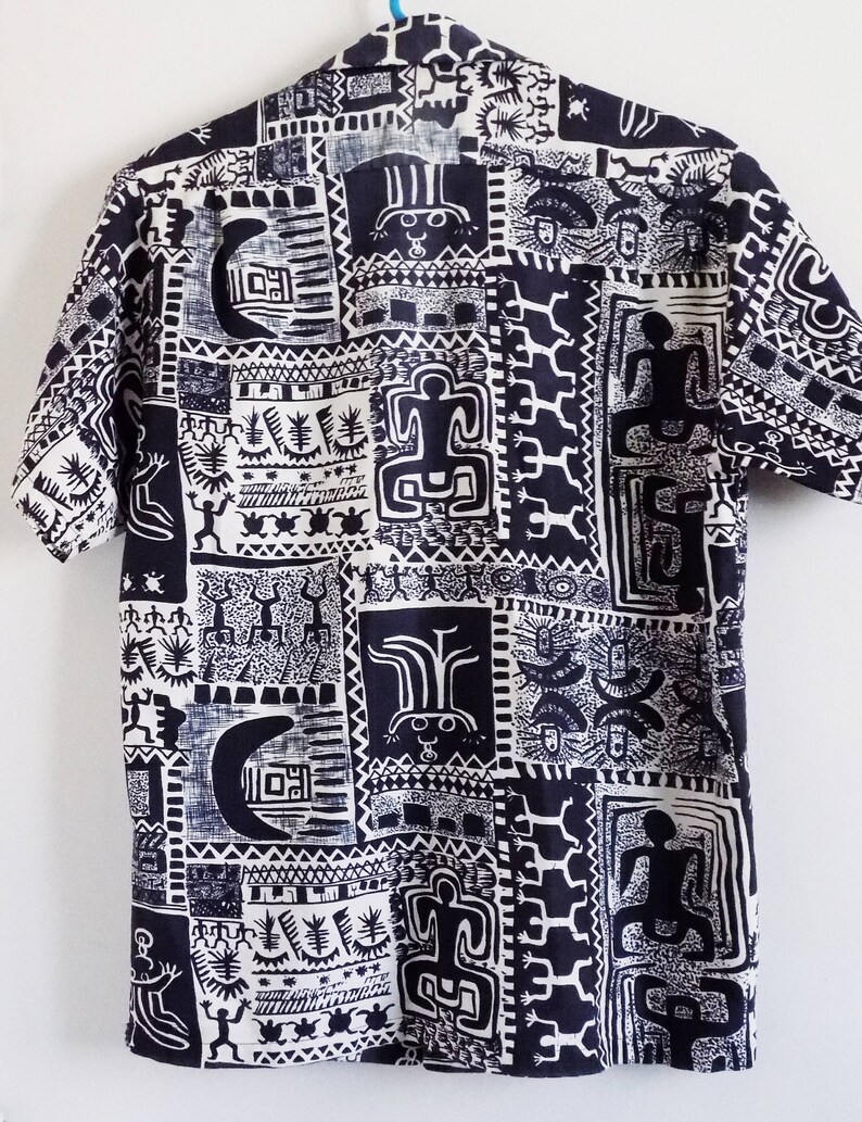 Pu&ograve; includere: Una camicia a maniche corte bianca e nera con un motivo geometrico. Il motivo presenta figure e simboli stilizzati.