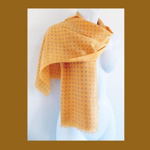 Könnte beinhalten: Ein gelber Schal mit einem kleinen, sich wiederholenden Blumenmuster. Der Schal ist an den Enden gefranstet.