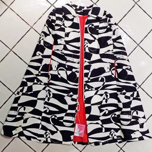 May include: A black and white patterned jacket with a red interior. The jacket features a unique design with abstract shapes and lines. The jacket is open, revealing the red lining and a tag.