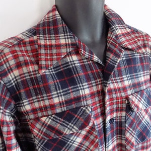 May include: A red, white, and blue plaid flannel shirt with long sleeves and two chest pockets.