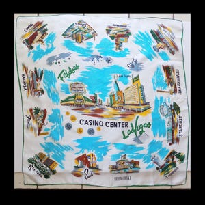 May include: A white cotton handkerchief with a colorful illustration of the Las Vegas Strip. The illustration includes the names of various casinos, including the Stardust, Riviera, and Showboat. The text "Casino Center Las Vegas" is printed in the center of the handkerchief.