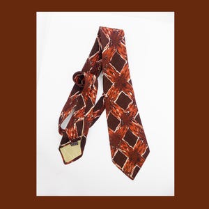 May include: A brown and orange patterned silk tie. The tie has a geometric design with a white background.