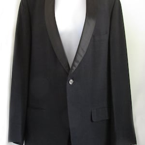 May include: A black tuxedo jacket with a satin lapel. The jacket has a single button fastening and a pocket on the left side.
