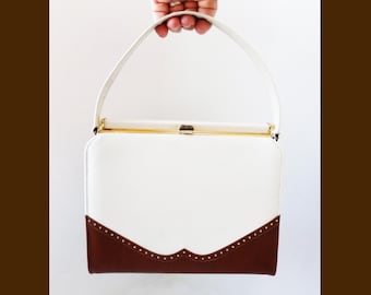 May include: A vintage white handbag with a brown bottom section and a white handle. The bag has a gold-colored clasp and trim. The brown section has a decorative scalloped edge with small white dots.