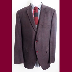 May include: A brown plaid blazer with a single button closure and red buttons. The blazer has a notched lapel and a pocket on the left chest.