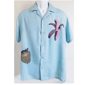 Puede incluir: Una camisa de manga corta de color azul claro con botones y un estampado geom&eacute;trico de pl&aacute;tano y fresa.