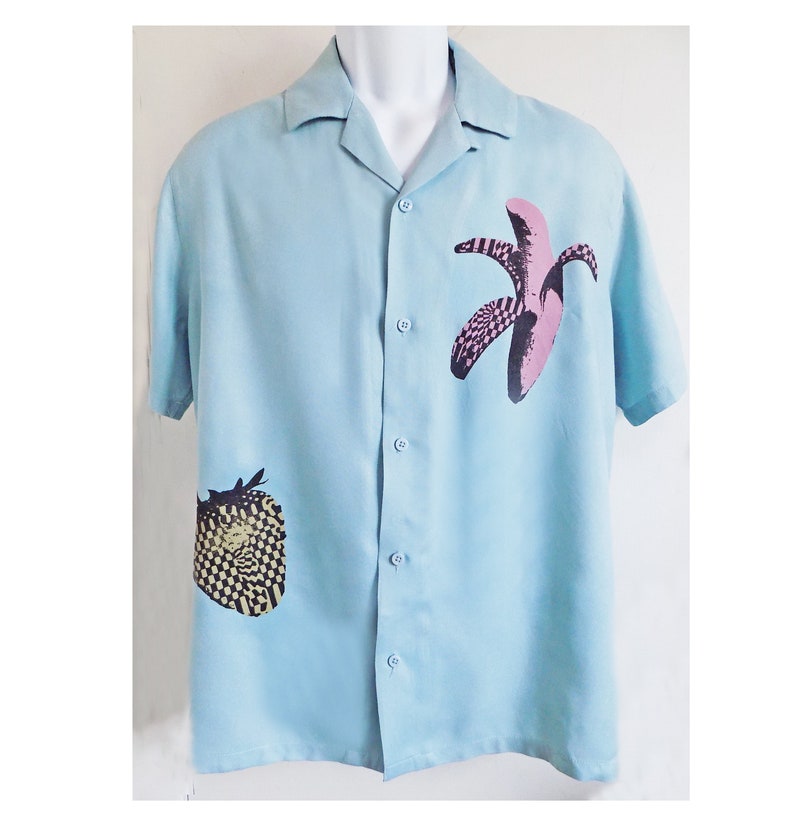 Puede incluir: Una camisa de manga corta de color azul claro con botones y un estampado geom&eacute;trico de pl&aacute;tano y fresa.