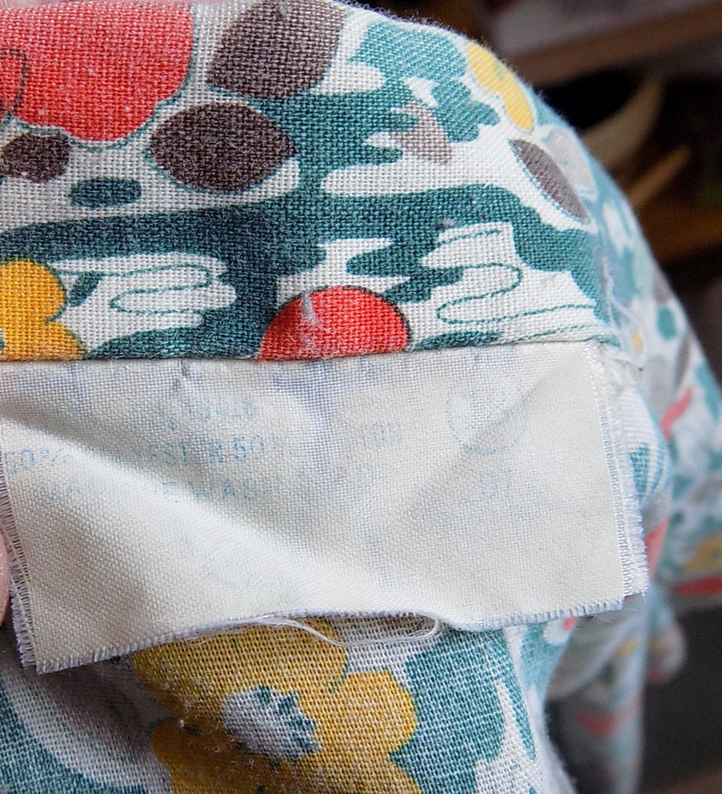 Puede incluir: Primer plano de una tela con un estampado floral colorido. La tela es de color verde azulado, amarillo, rojo y marr&oacute;n. Una etiqueta blanca est&aacute; cosida a la tela con un texto demasiado borroso para leer.