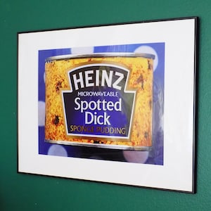 May include: A Heinz brand can of spotted dick sponge pudding. The can is yellow with black and red text. The text reads "Heinz Microwaveable Spotted Dick Sponge Pudding".