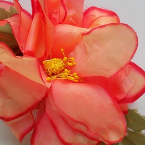 May include: A large, pink fabric flower with a yellow center. The flower has a ruffled edge and is made of a soft, silky material.