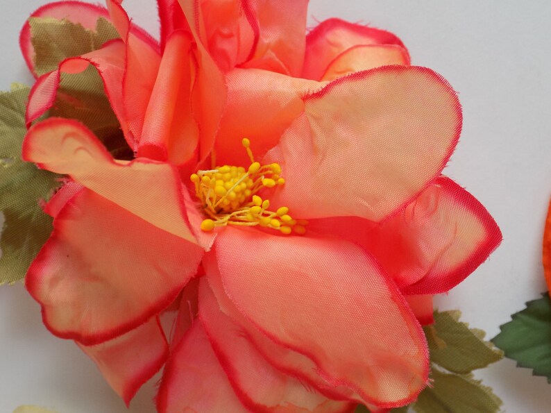 May include: A large, pink fabric flower with a yellow center. The flower has a ruffled edge and is made of a soft, silky material.