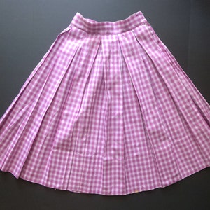 May include: A pleated skirt in a pink and white gingham pattern. The skirt has a wide waistband and a full, flowing silhouette.