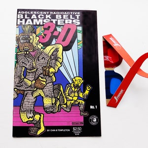 May include: A comic book cover with a black background and colorful illustrations. The title is "Adolescent Radioactive Black Belt Hamsters 3-D". The cover features three cartoon characters running. The comic book is number one and costs $2.50. A pair of red and blue 3D glasses are included.