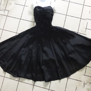 May include: A black strapless dress with a full skirt. The dress is made of a smooth, silky fabric and has a fitted bodice.