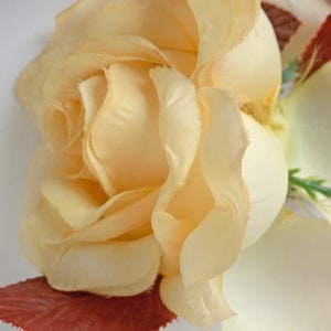 May include: A close-up of a pale yellow silk rose with a red velvet base. The rose is in focus, while the background is blurred.