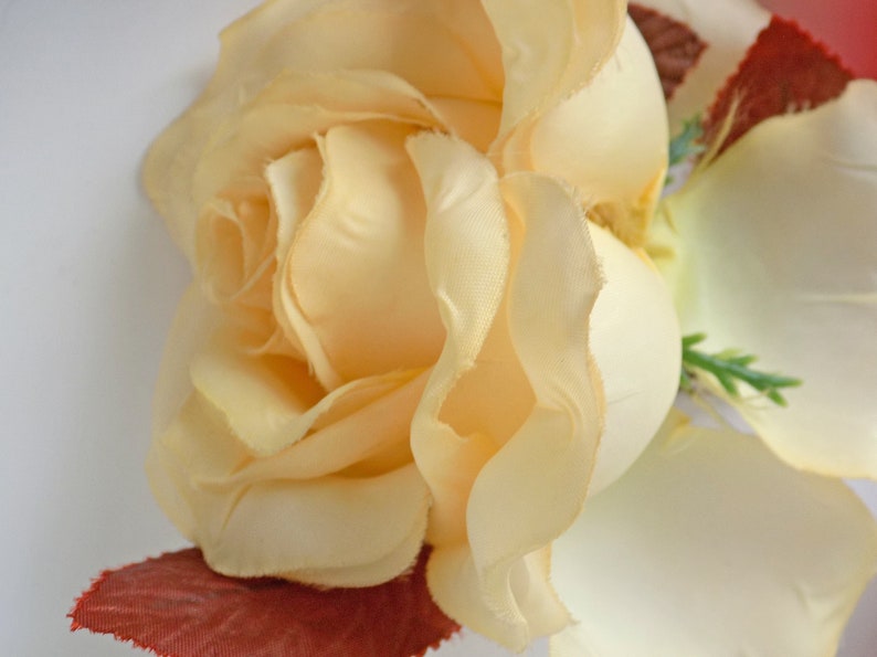 May include: A close-up of a pale yellow silk rose with a red velvet base. The rose is in focus, while the background is blurred.