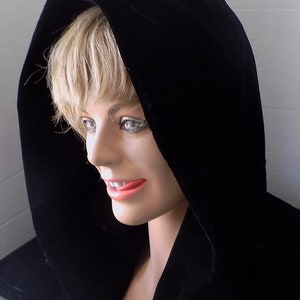 May include: A black velvet hooded cloak with a soft, flowing fabric. The hood is pulled up over the head, and the cloak is draped over the shoulders.