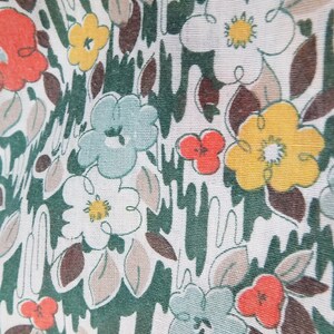 Puede incluir: Una tela blanca con un patr&oacute;n floral verde, marr&oacute;n y amarillo. Las flores son estilizadas y tienen un aspecto retro.