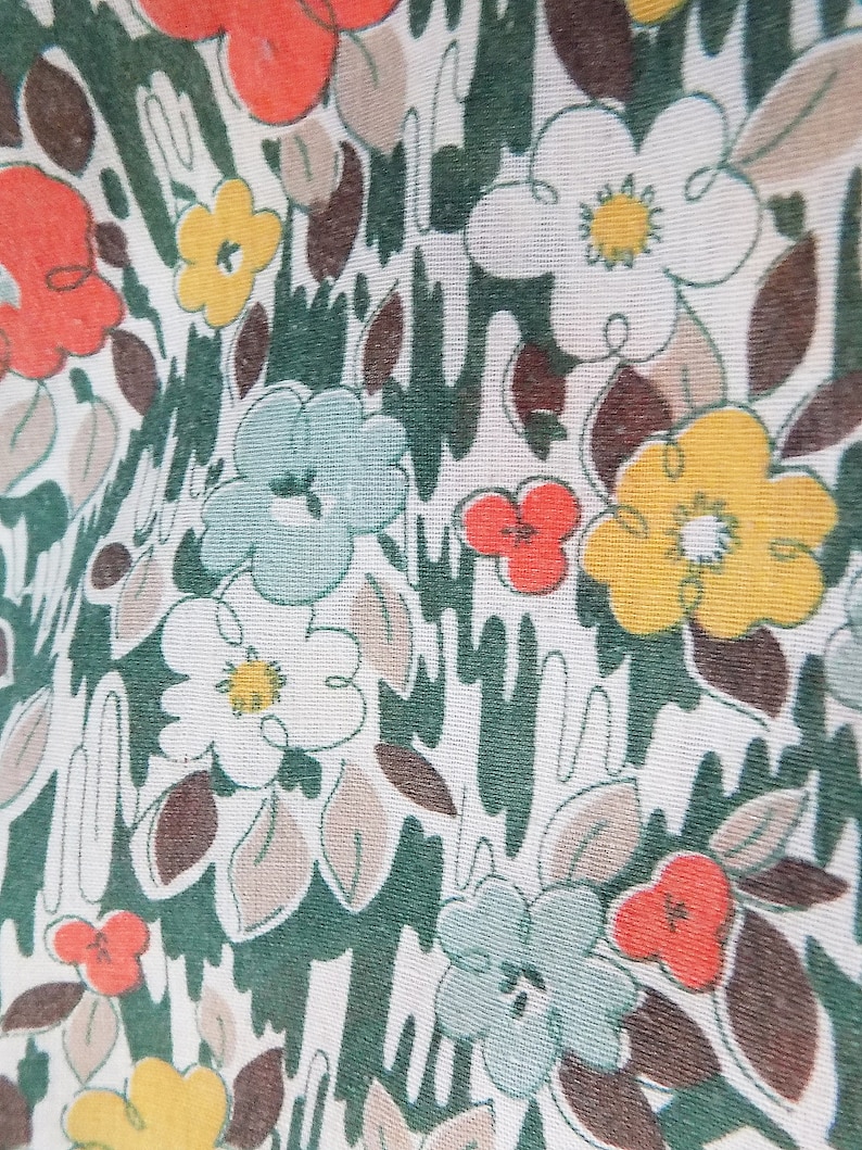 Puede incluir: Una tela blanca con un patr&oacute;n floral verde, marr&oacute;n y amarillo. Las flores son estilizadas y tienen un aspecto retro.