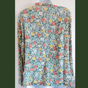 Puede incluir: Una camisa de manga larga con fondo verde y un estampado floral en tonos naranja, amarillo y blanco.