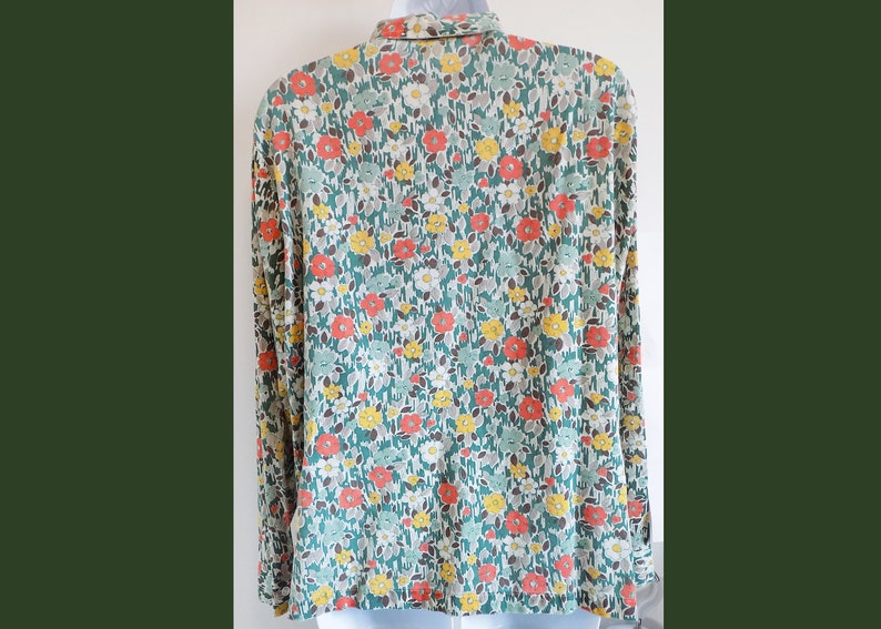 Puede incluir: Una camisa de manga larga con fondo verde y un estampado floral en tonos naranja, amarillo y blanco.