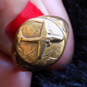 May include: A gold ring featuring a detailed image of an aeroplane on the face of the ring.