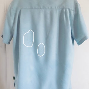 Puede incluir: Una camisa de manga corta azul claro con dos marcas blancas tenues en la espalda.