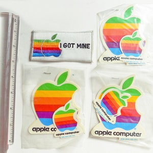 Może przedstawiać: Zestaw vintage naklejek Apple Computer z logo tęczowej jabłka. Naklejki są w różnych rozmiarach i zawierają tekst "I GOT MINE", "apple" i "apple computer".