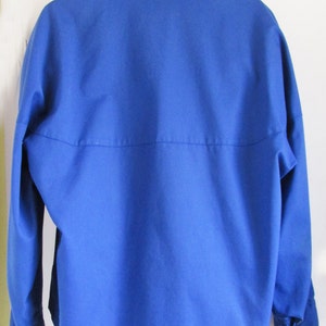 Puede incluir: Una chaqueta azul s&oacute;lido con cuello alto y mangas largas. La chaqueta tiene cierre de botones y dos bolsillos en la parte delantera.