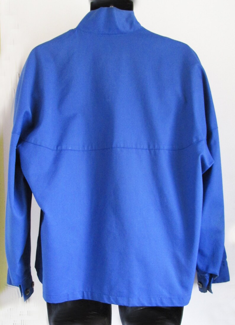 Puede incluir: Una chaqueta azul s&oacute;lido con cuello alto y mangas largas. La chaqueta tiene cierre de botones y dos bolsillos en la parte delantera.