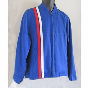 Puede incluir: Una chaqueta azul con una franja blanca y roja en la manga.