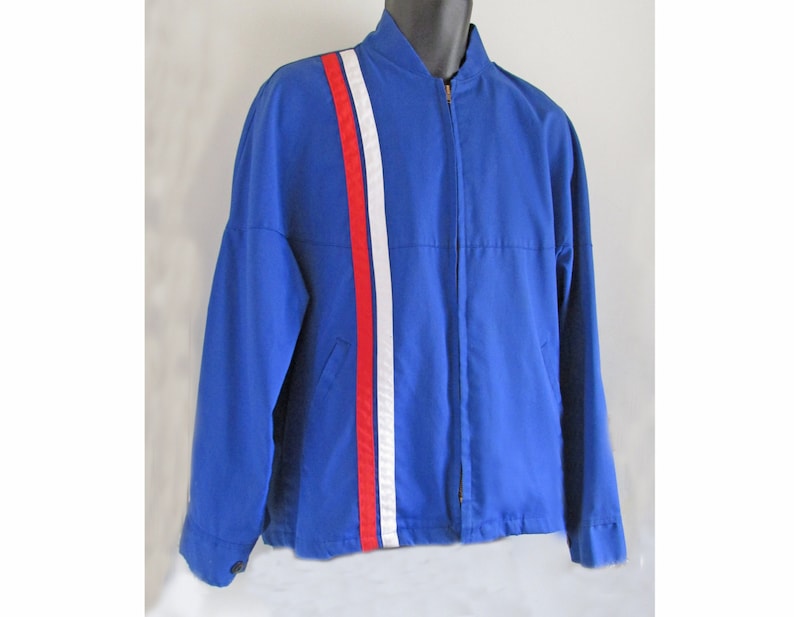 Puede incluir: Una chaqueta azul con una franja blanca y roja en la manga.