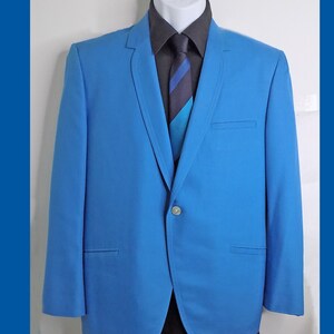 May include: A light blue blazer with a single button closure. The blazer has a notched lapel and a pocket on the left side. The blazer is worn over a dark gray shirt with a blue and white striped tie.