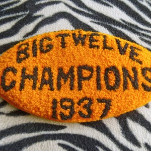 Op de afbeelding: Oranje vilt patch met zwarte geborduurde tekst die "BIG TWELVE CHAMPIONS 1937" luidt.