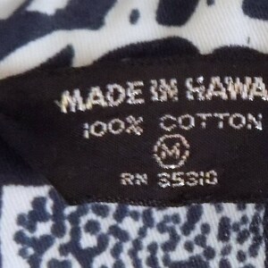 Pu&ograve; includere: Etichetta bianca e nera con il testo "Made in Hawaii 100% Cotton RN 35310" e una taglia "M" in un cerchio.