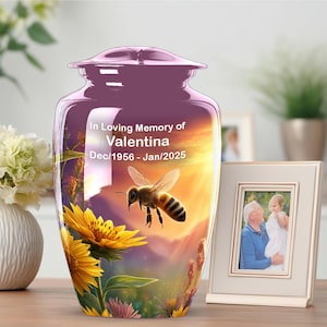 May include: A purple cremation urn featuring a printed scene of a honeybee flying over yellow sunflowers at sunset. The text reads In Loving Memory of Valentina Dec/1956 - Jan/2025. The urn has a smooth, glossy finish and a matching removable lid.
