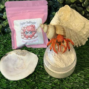 May include: A pink pouch of oyster shell powder with a cartoon hermit crab graphic, a jar of powder, a hermit crab figurine, and seashells on green turf. The text on the pouch reads "Oyster Shell Powder" and "Hermit Crab Nerd."