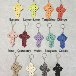 Pode incluir: Chaveiros de cruz de crochê em várias cores: amarelo, verde, laranja, vermelho, rosa, bordô, roxo, verde-azulado, azul, bege, branco, cinza e preto. Cada cruz tem um chaveiro prateado, com nomes de cores.