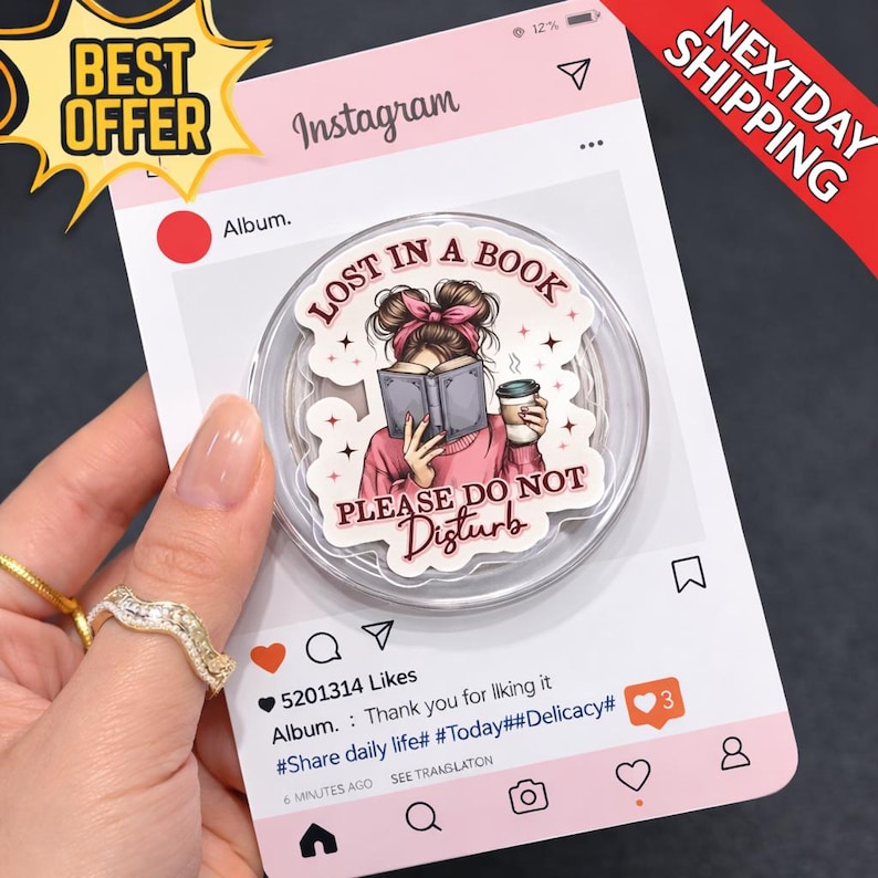 Puede incluir: Un soporte transparente para tel&eacute;fono con un gr&aacute;fico de una mujer leyendo un libro y sosteniendo una taza de caf&eacute;, con el texto "LOST IN A BOOK PLEASE DO NOT DISTURB". El soporte est&aacute; sobre un fondo rosa con tem&aacute;tica de Instagram.