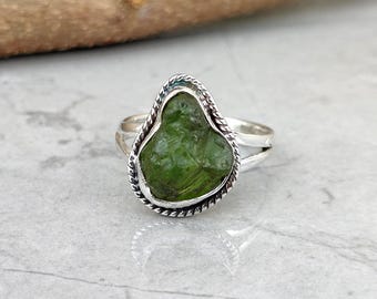 May include: A sterling silver ring featuring a large, irregularly shaped, vibrant green gemstone. The stone is set within a decorative, twisted rope-like border. The ring's band is split at the top, adding to its unique design.