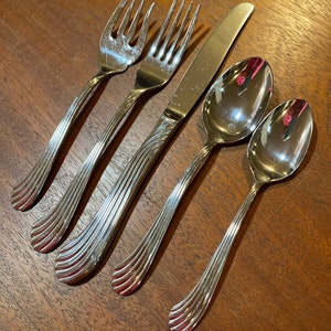 May include: Five pieces of silverware, including two forks, a knife, and two spoons, all with a silver finish and a wavy, textured handle.