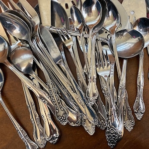 May include: A collection of silver cutlery, including spoons, forks, and knives, with ornate handles. The cutlery is arranged in a random pattern, with some pieces overlapping.
