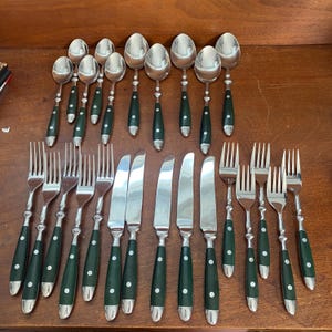 May include: A flatware set consisting of stainless steel spoons, forks, and knives. Each piece features a dark green handle secured with two silver-toned rivets. The set includes various sizes of spoons, dinner forks, and dinner knives.