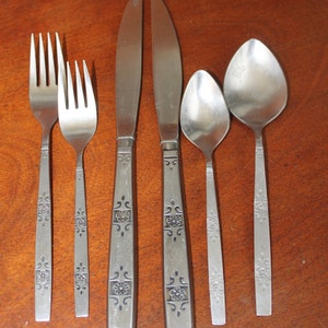 May include: Set of six silver-toned flatware with a floral design on the handles. The set includes two forks, two knives, and two spoons.