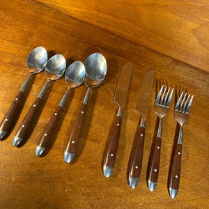 May include: Set of eight silver-toned flatware with brown wooden handles. The set includes four spoons, two forks, and two knives.