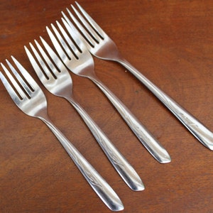 May include: Four silver forks with ornate designs on the handles. The forks are arranged in a row, with the handles pointing to the right.