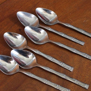 May include: Six silver spoons with bamboo-inspired handles. The spoons are arranged in a row, with the handles pointing to the right.