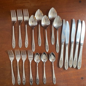 May include: A set of 18 silver-toned flatware pieces, including forks, spoons, and knives. The flatware has a simple design with a floral pattern and the word "18/10" engraved on each piece.