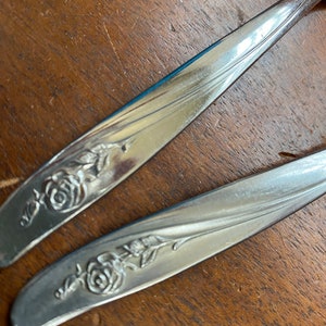 May include: Two silver-plated butter knives with a rose design on the handle.
